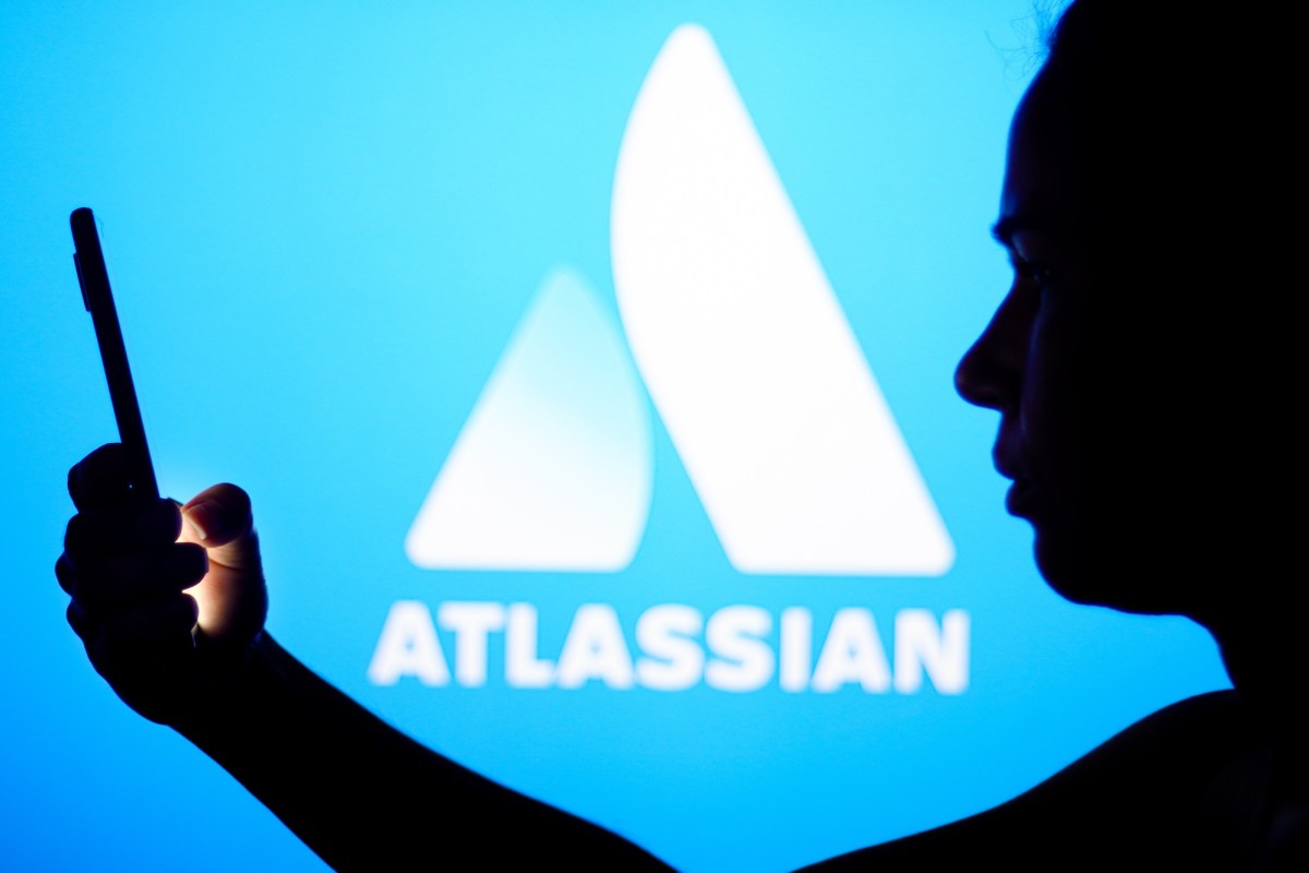 an Atlassian logo on a blue background with a person silhouetted in front holding a phone, for some reason