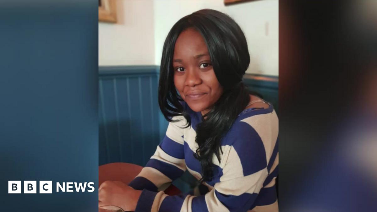 Chanel Thompson sits at a table in a café, wearing a blue and white striped top, looking at the camera.