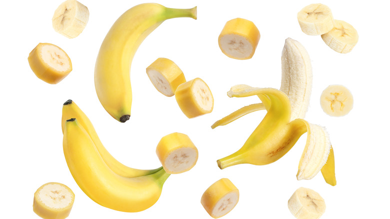 Whole, peeled, and cut bananas swirling against a white background