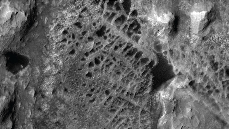 Gray terrain seen from above with web-like intersecting ridges and dark patches.