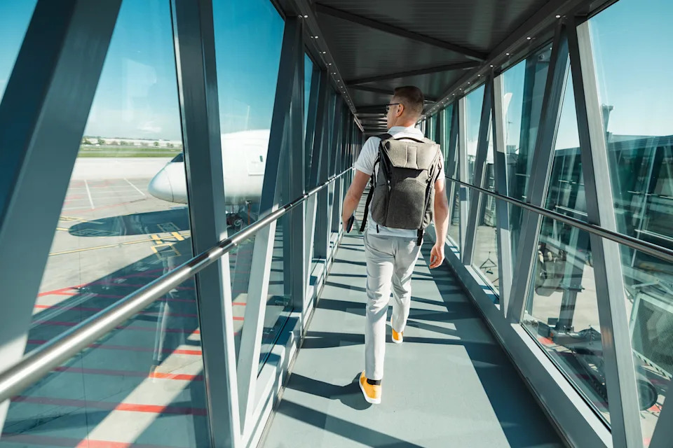 Person walking through airport jet bridge toward airplane, carrying a backpack, suggesting travel or business trip