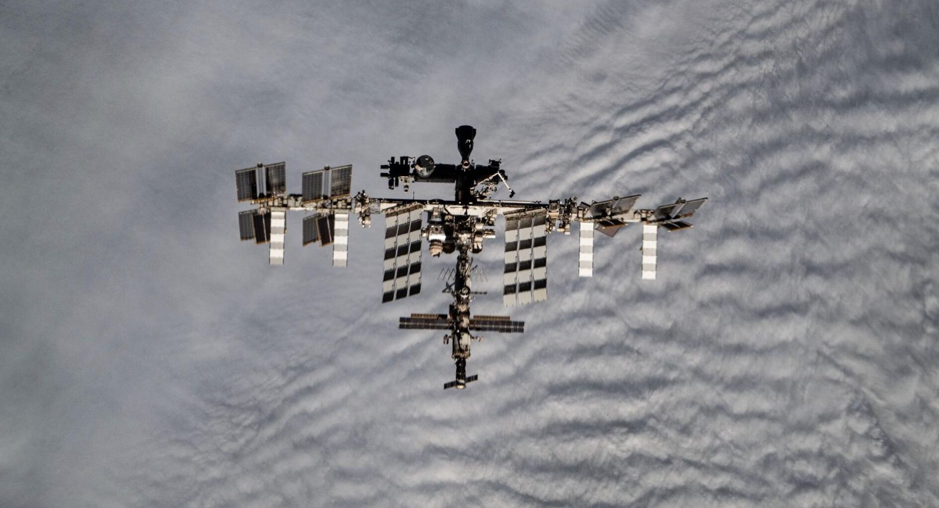 long-distance shot of the international space station from above, with cloudy earth skies in the background