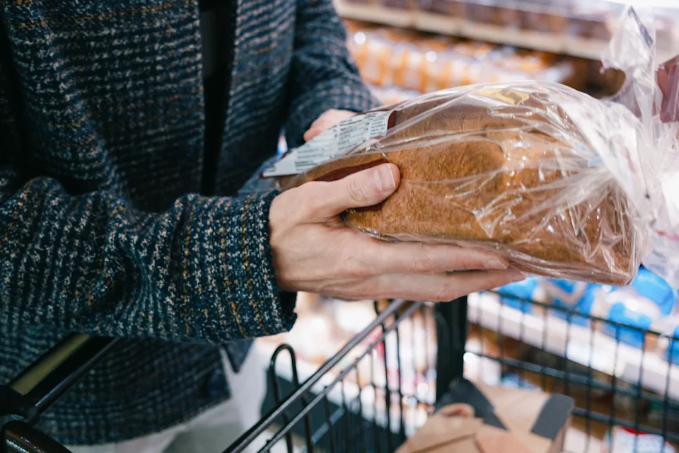 Person holding a packaged loaf of bread over a shopping cart in a grocery store