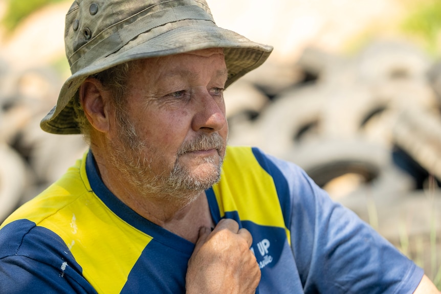 Man with wide brim hat looks to the right with a pile of tyres behind him.