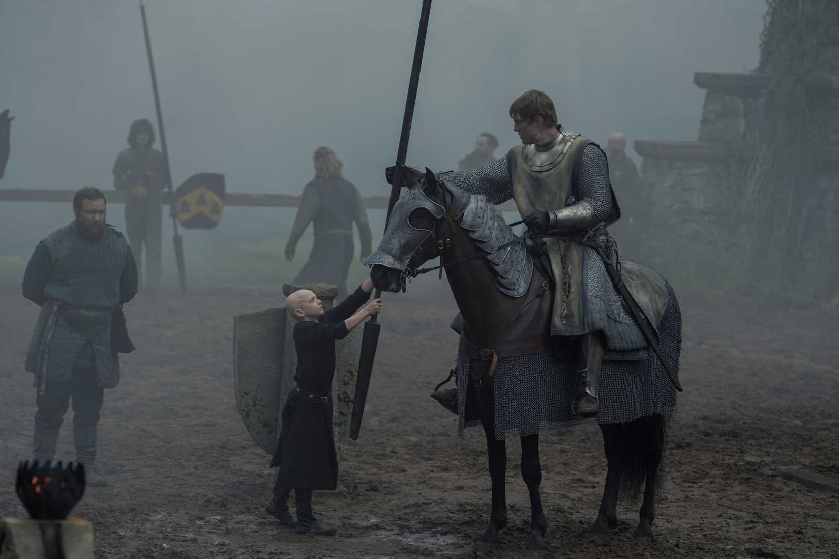 A knight on horseback (Peter Claffey) accepts a lance from a small bald boy (Dexter Sol Ansell) in a foggy jousting arena in A Knight of the Seven Kingdoms