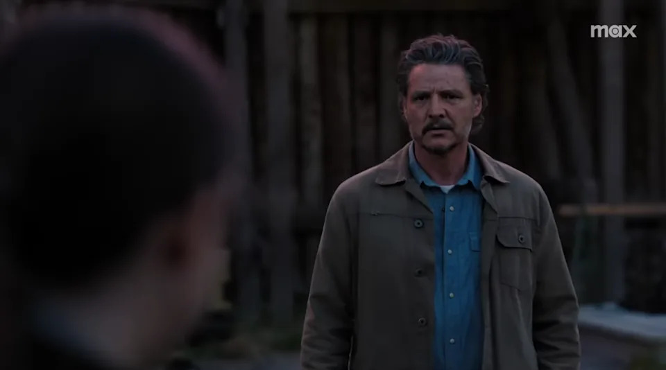 A person with a concerned expression stands outdoors wearing a casual jacket and shirt