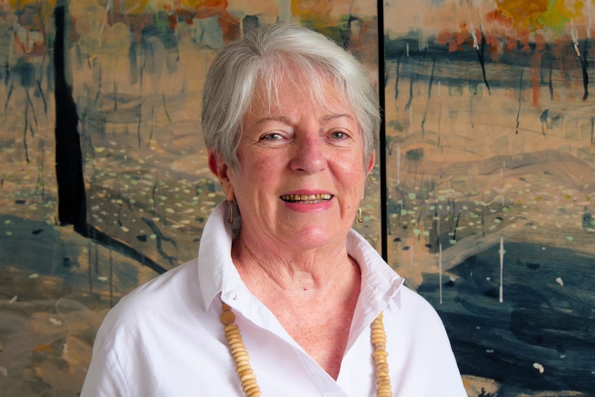 A woman dressed in a collared shirt, standing in front of a bright painting