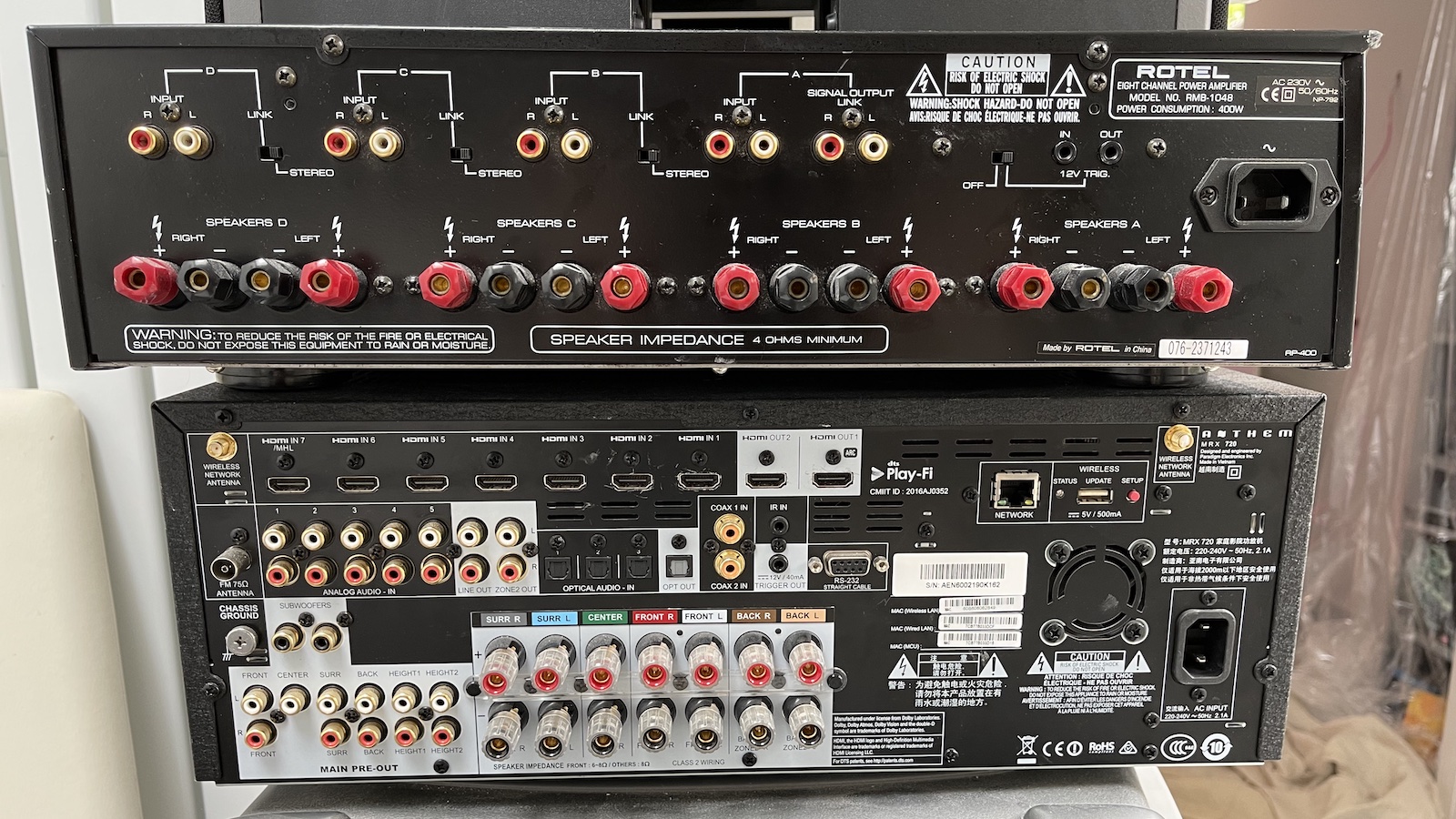 A photo of a Rotel power amp stacked on top of a an Anthem AVR, showing the arrays of connections on the rears of both