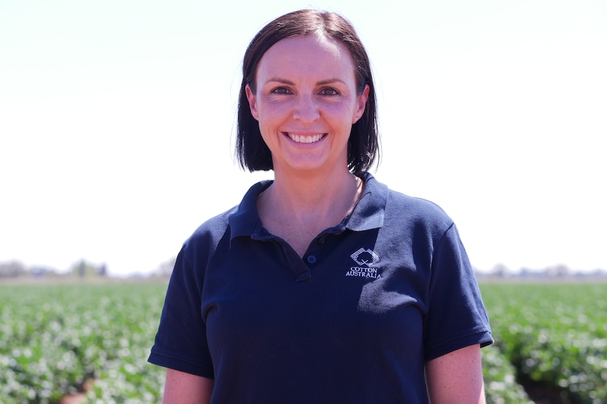 A woman with brown hair smiles at the camera with rows of cotton in the background.