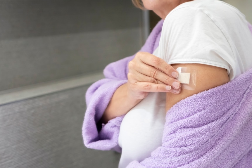 A woman's arm, jumper off shoulder as she places on a transdermal estrogen patch.
