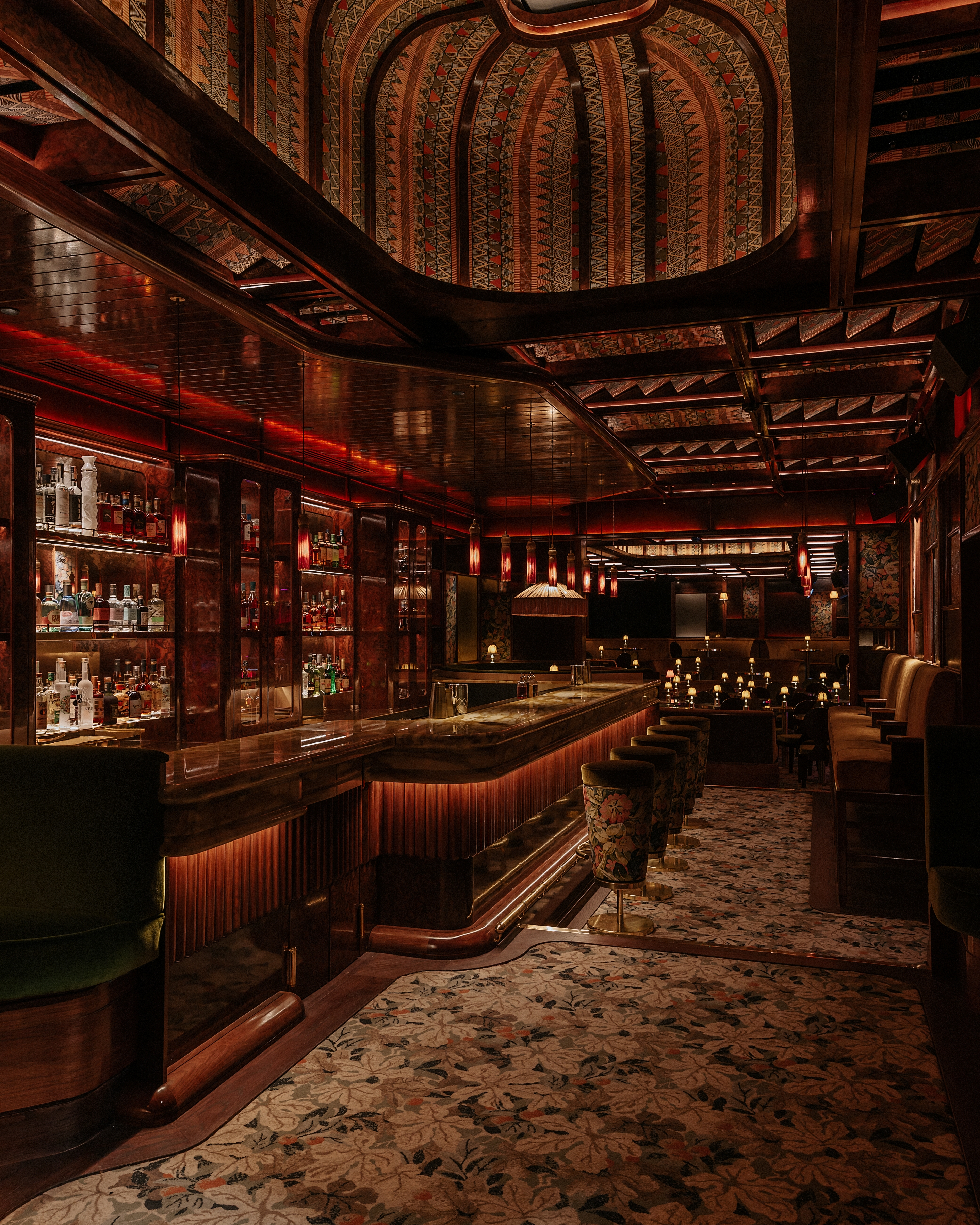 A dimly lit, textiles and lacquered wood-clad jazz club with lots of softly glowing table lamps, performers playing live, and a red-tinted light.