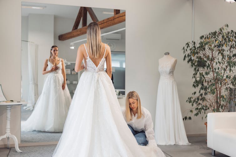 A bride trying on a wedding dress in a boutique, with a consultant adjusting the gown.