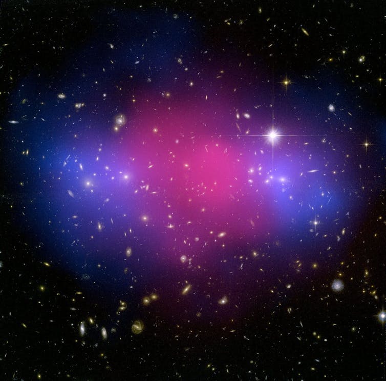Clouds of blue and pink shown, with lots of bright spots representing galaxies shown in the background.