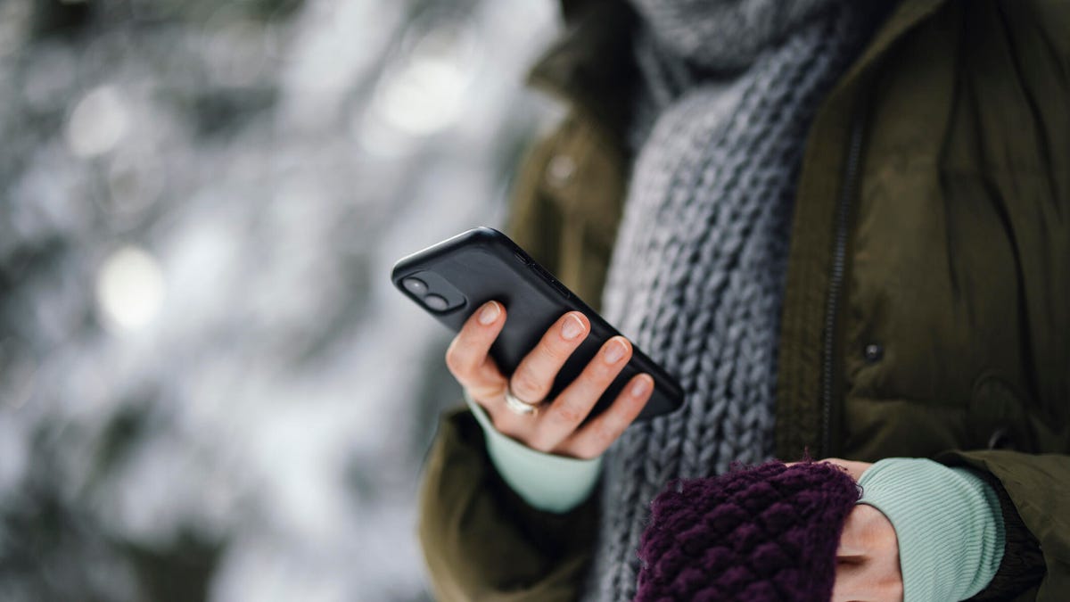A person holding a smartphone in cold weather.
