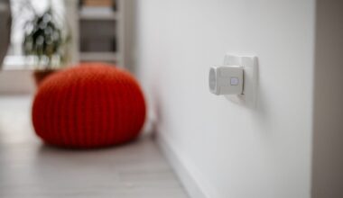 A smart plug plugged into a white home wall in front of an orange cushion.