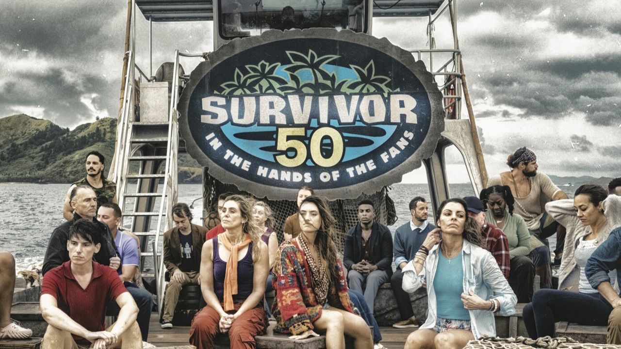 The cast of Survivor season 50 gathered under a sign that says 'Survivor 50 In the Hands of the Fans'.