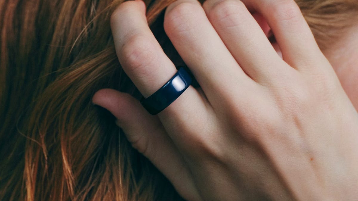 A close-up of the navy Oura Ring on a hand running through red hair.
