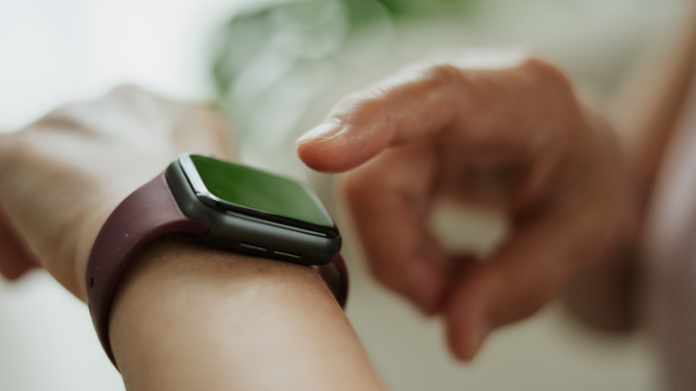 An individual's right hand pointing with their index finger at a smartwatch that's on their left wrist