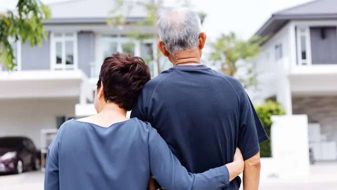 A senior couple embracing each other outside a home as they weigh downsizing their home during retirement.
