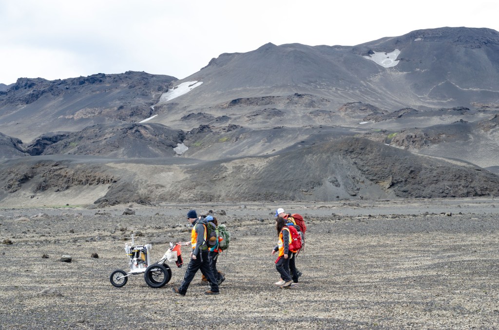 Artemis II science trainers push a lunar tool cart across the lunar-like landscape of Iceland during an Artemis II crew geology field training.
