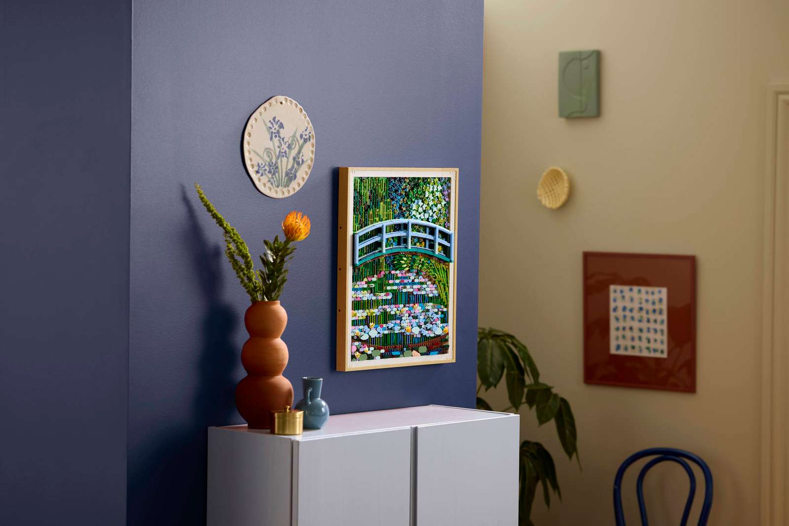 The ‘Monet Bridge Over a Pond of Water Lilies’ LEGO set hanging on a purple wall above a cabinet