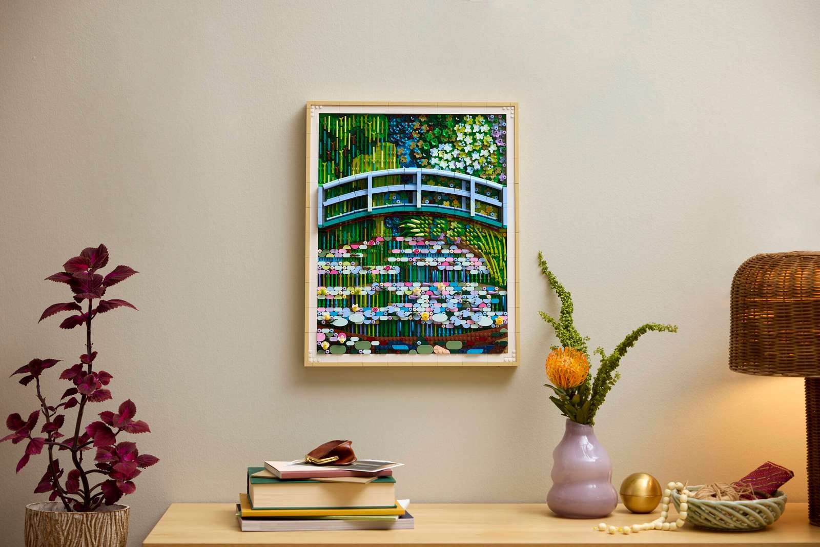 The ‘Monet Bridge Over a Pond of Water Lilies’ LEGO set hanging on a wall above a shelf with books, vases, and lamps