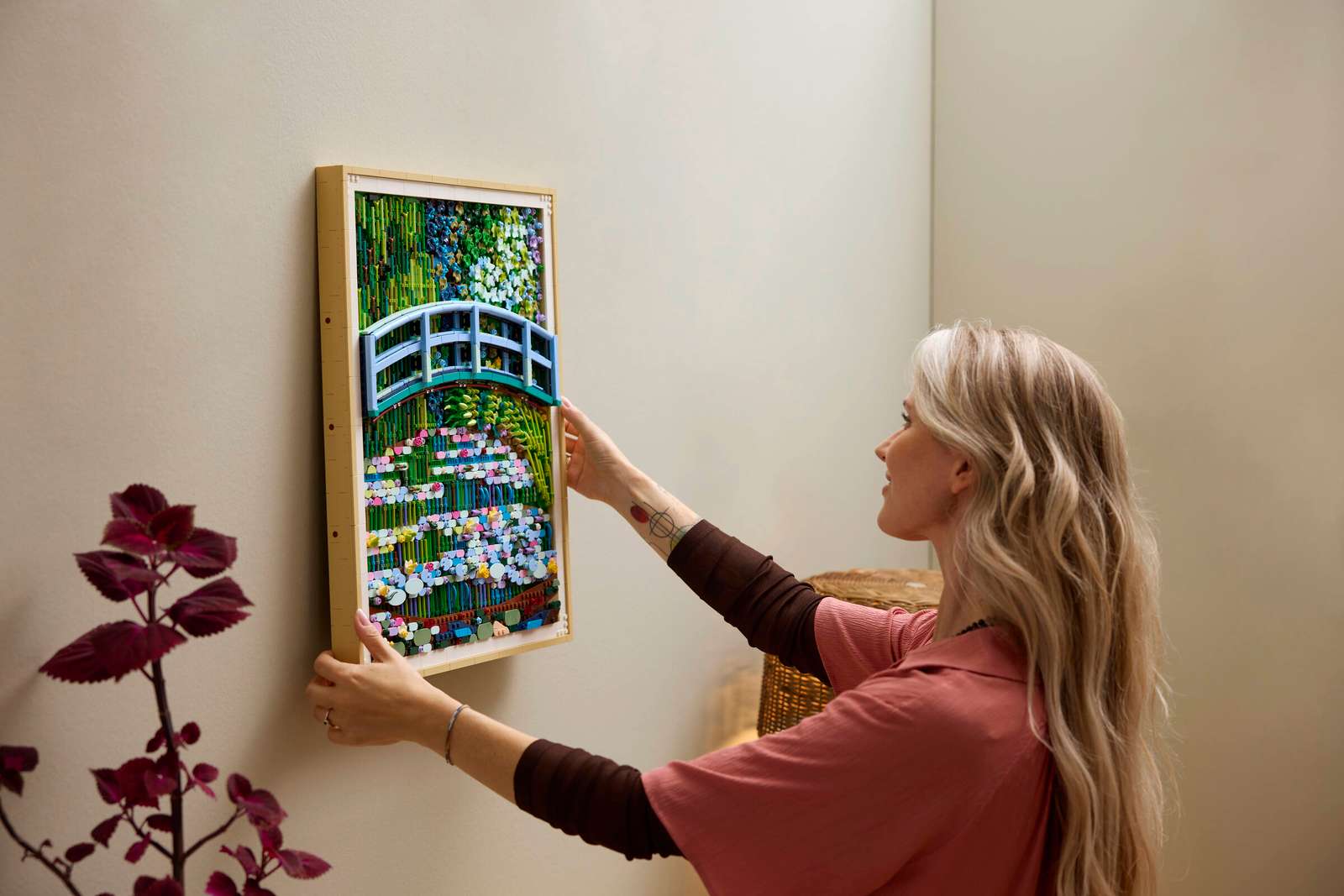 A woman hanging up the ‘Monet Bridge Over a Pond of Water Lilies’ LEGO set on a white wall