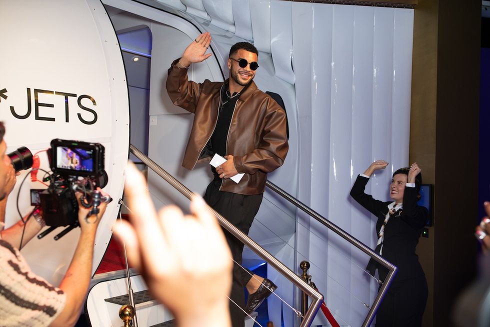 Man in brown jacket waves from stairs with cameras focused on him - Fame Factory experience
