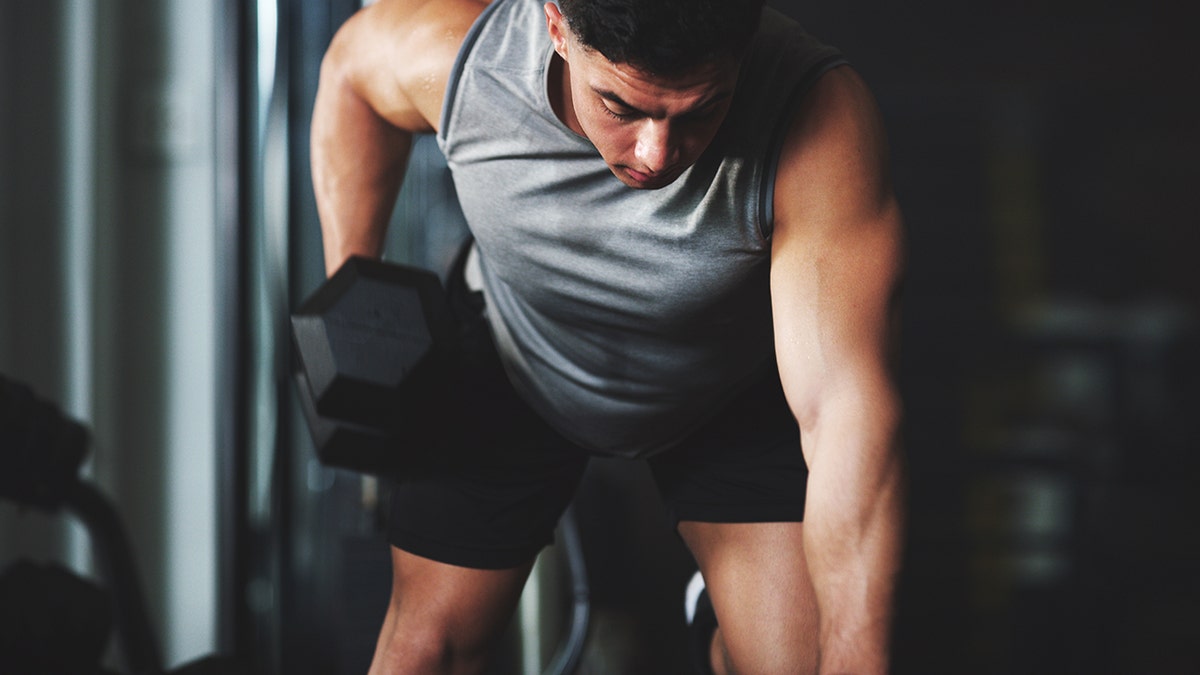 Shot of a sporty young man exercising with a dumbbell at the gym