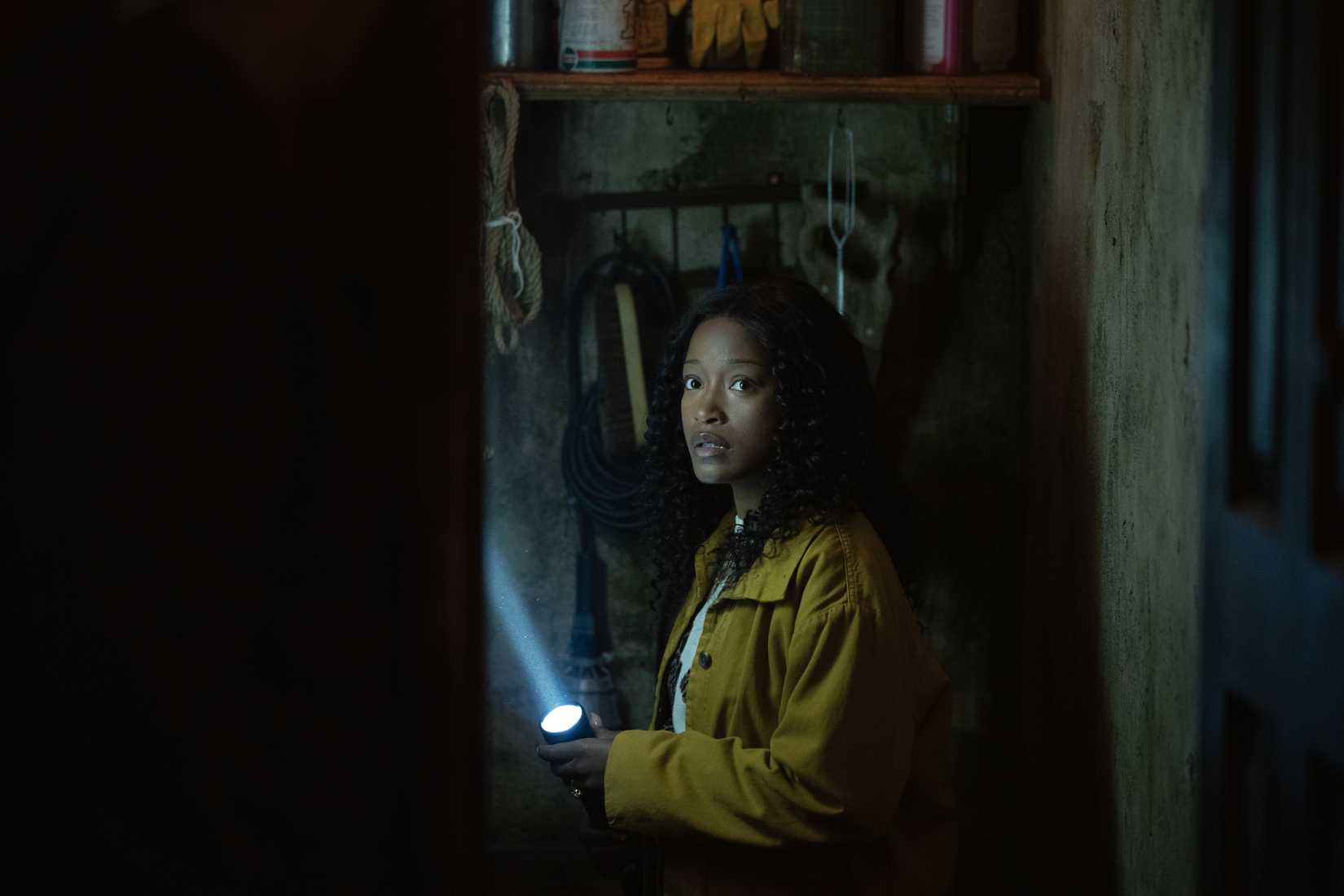 Keke Palmer holds a flashlight and looks scared in an image from The Burbs