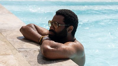 A man rests his arms on the edge of a pool after swimming. 
