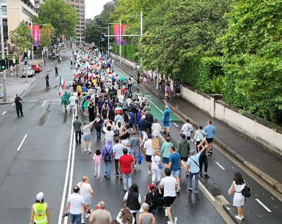 A large number of people march along a city street as police watch on.