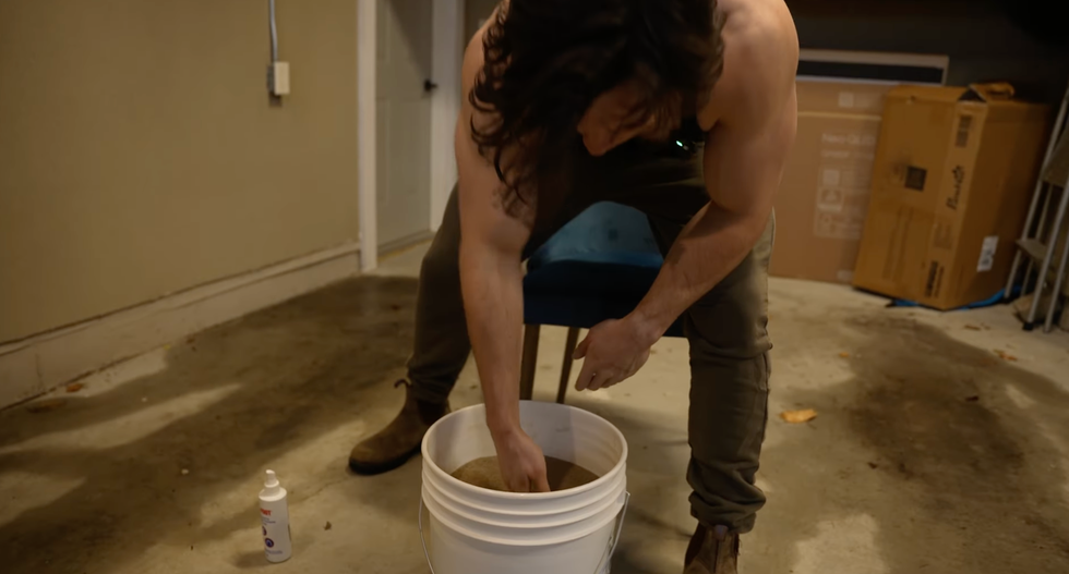person interacting with a bucket of material seated in a garage