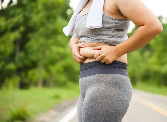 Fat women wear gray sports clothing and use their hands to squeeze excess fat. In the park want to lose weight