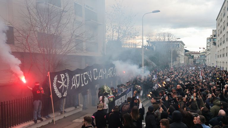 A man holds a flare next to banners reading: 'justice for Quentin' and 'goodbye comrade'. Pic: Reuters