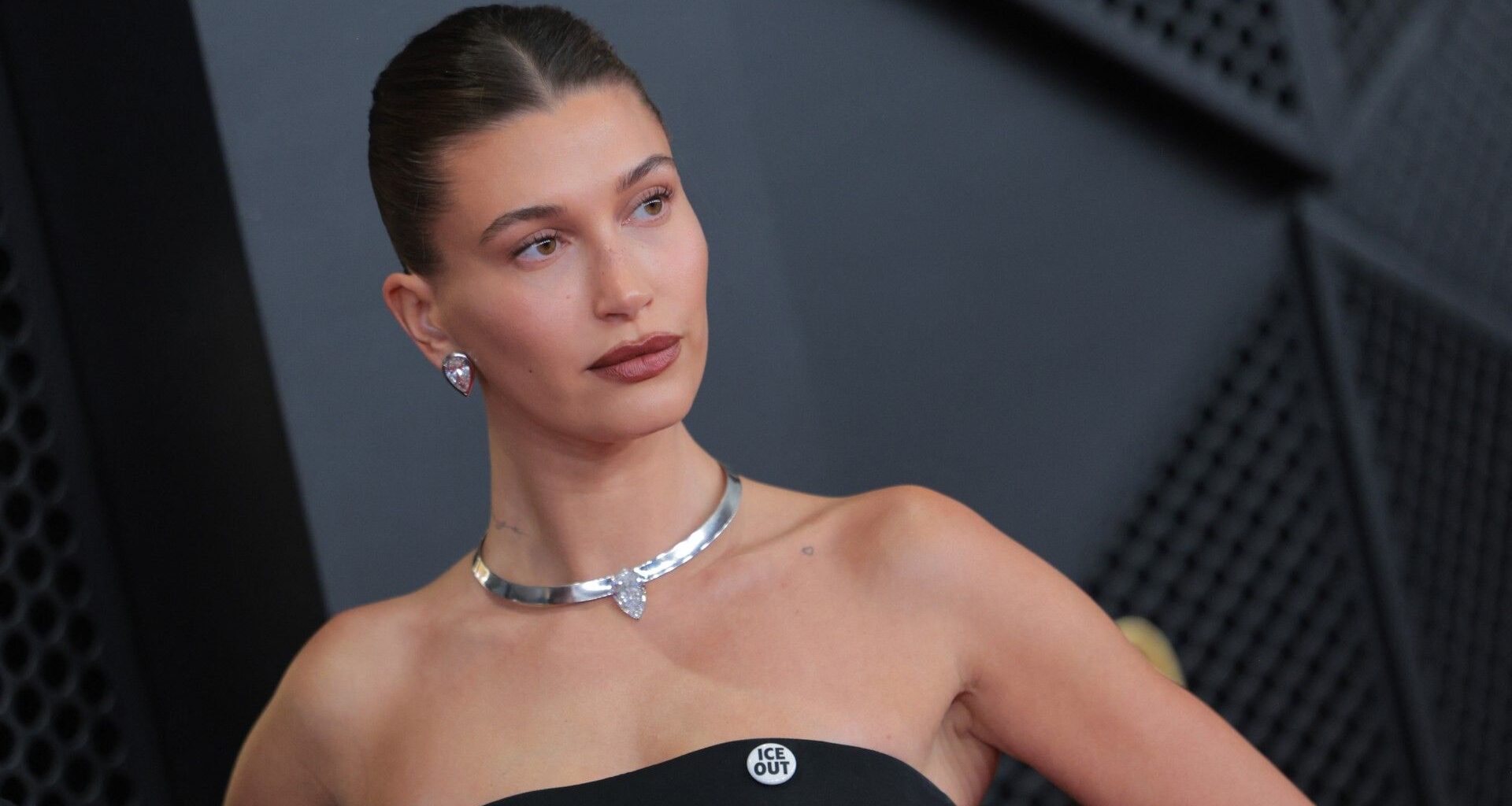 a white woman wears a strapless black gown and poses in front of a black background at a red carpet event