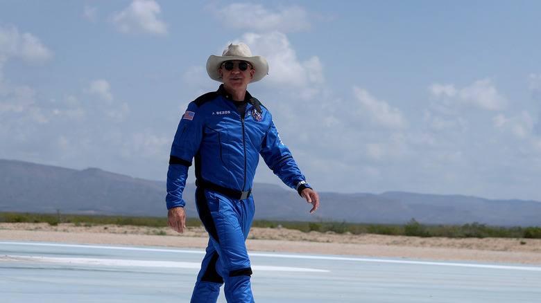 Jeff Bezos, clad in a Blue Origin space suit, cowboy hat, and sunglasses, strides across the tarmac in preparation of his flight in Blue Origin's famed New Shepard launch.