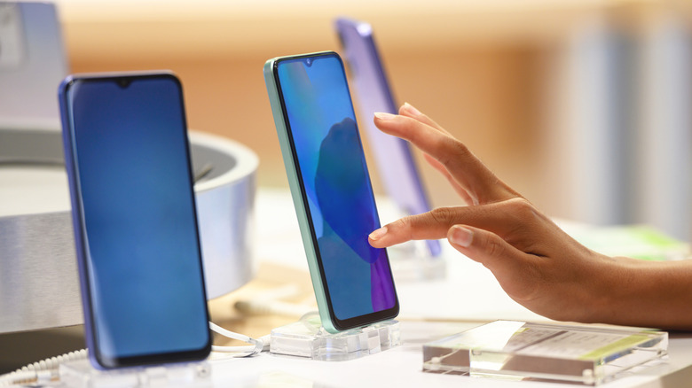 Hand interacting with smartphones displayed on a retail counter