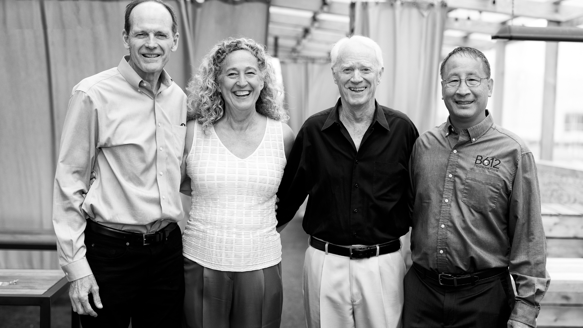 black and white photo of one woman and three men, all older, well-dressed and smiling
