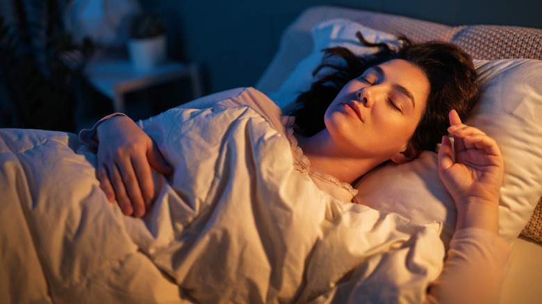 A woman sleeping in her bed in a dark room lit by a small lamp