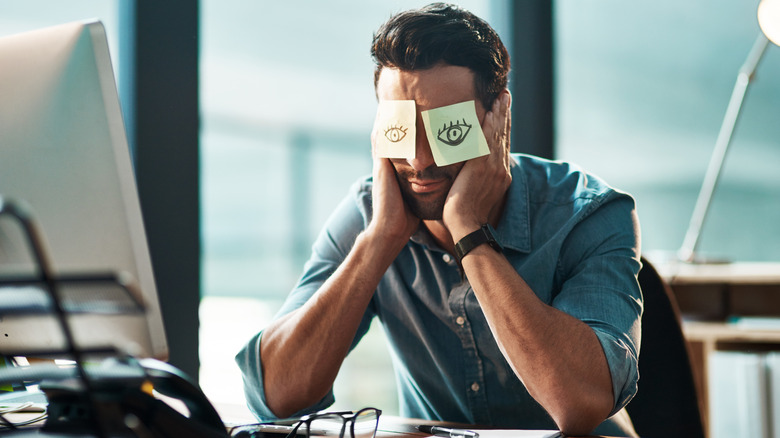 A tired man pretending to be awake at work with Post Its over his eyes