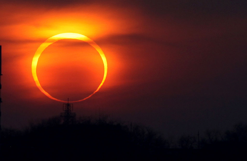 A ring of yellow light illuminates an orange streak in the dark sky during an annular solar eclipse