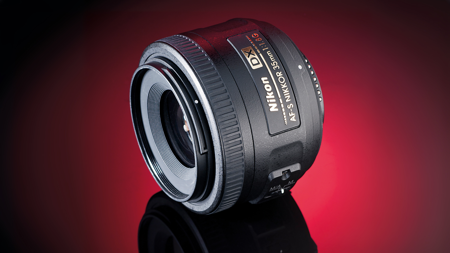 Close-up of a Nikon AF-S NIKKOR 35mm f/1.8 DX lens, showcasing its design against a gradient red background