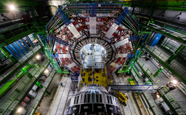 A view looking up at a hexagonal ring of red scaffolding, seen amidst a tall room with green vertical scaffolding around it