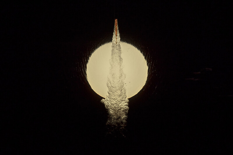 A rocket is launching directly in front of a full moon at night, with its bright exhaust plume illuminated against the dark sky and the moon’s light creating a dramatic silhouette.