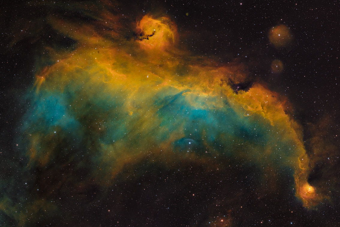 The Seagull Nebula, NGC 2032, appearing as golden and turquoise clouds against a dark, star-filled sky.
