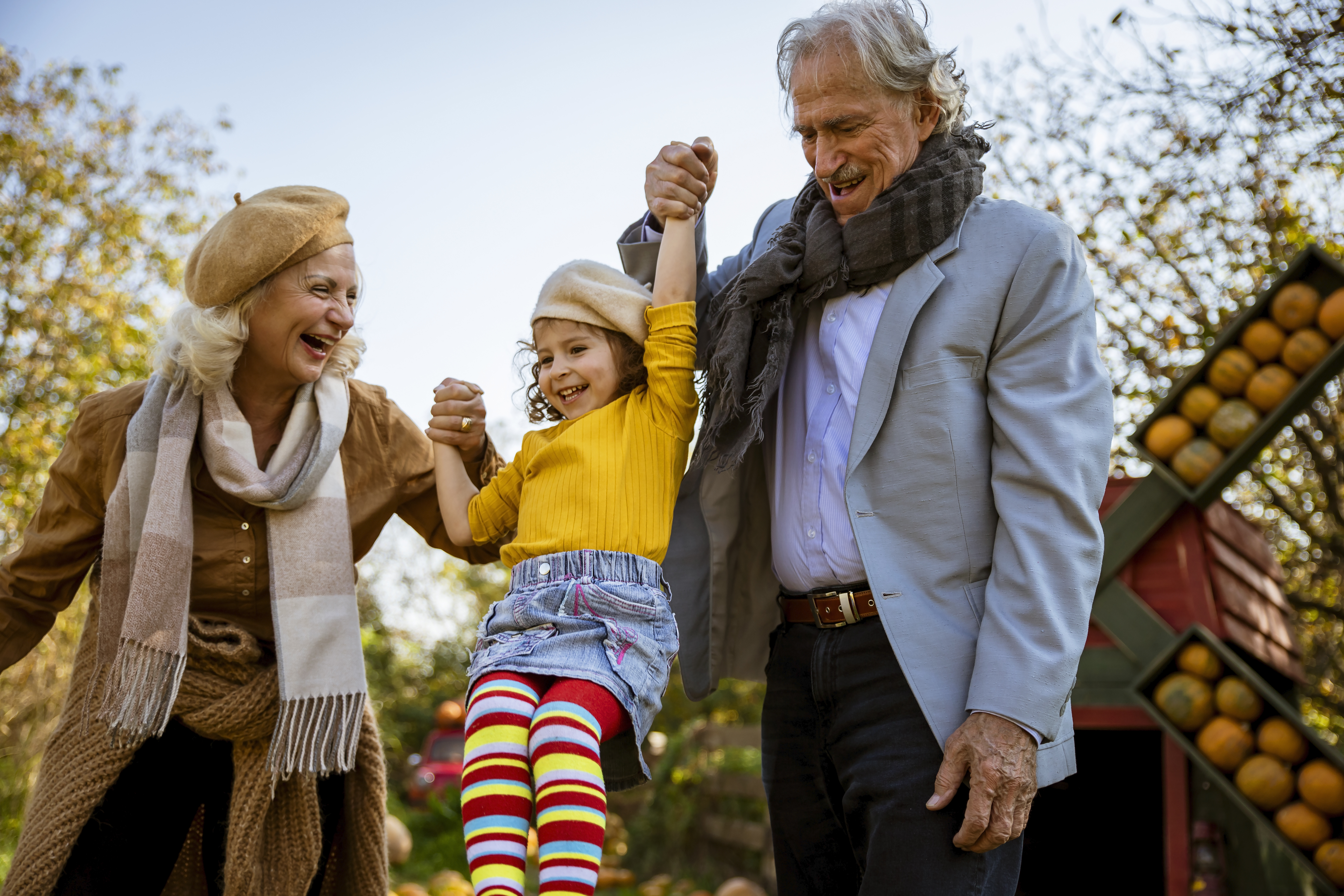 Grandparents playing with their granddaughter, swinging her in the air, in a pumpkin patch.