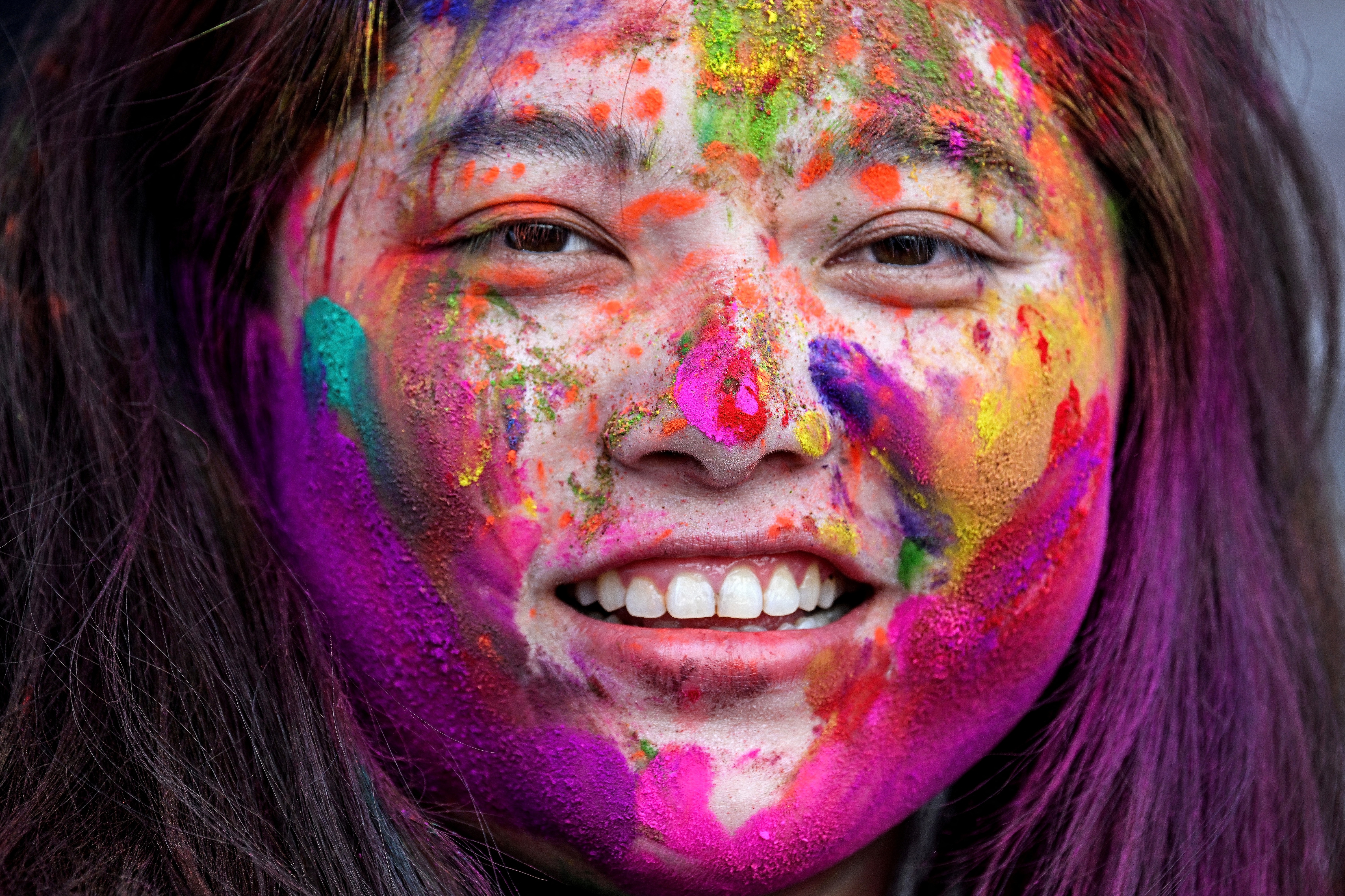 A woman smiles, her face covered in multi-colored powder during the Holi festival.