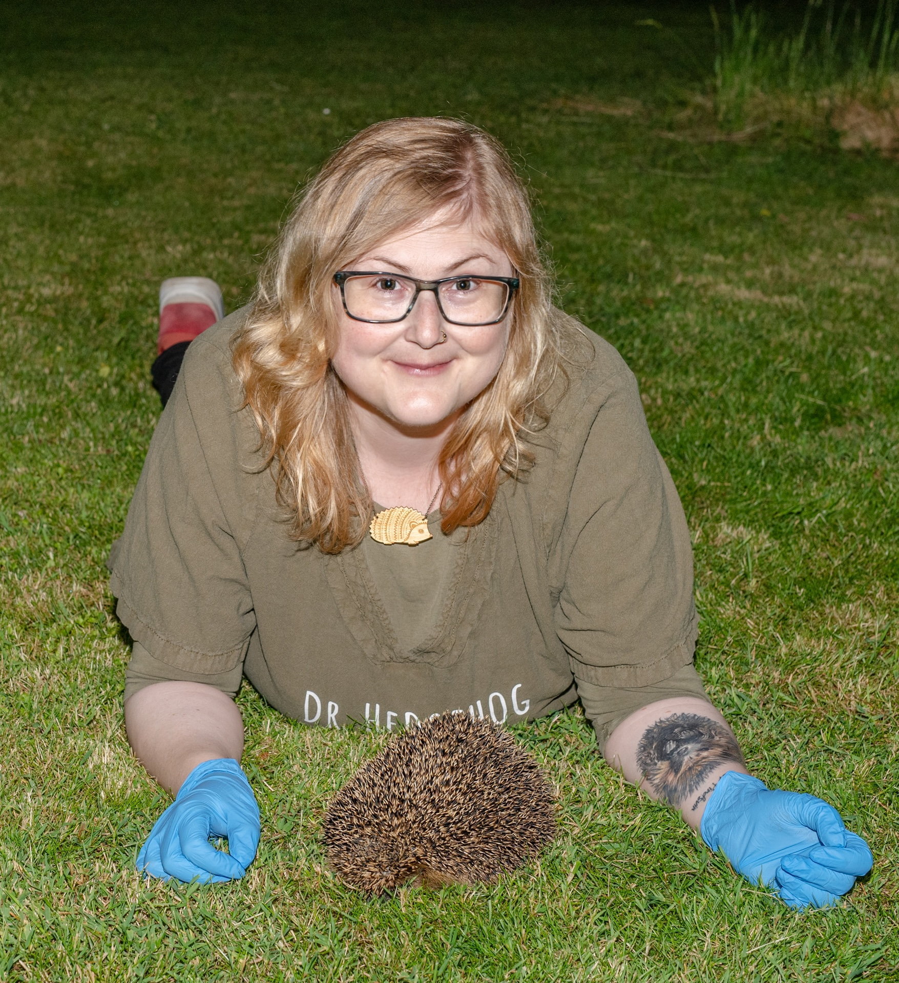 Dr. Sophie Lund Rasmussen lying on grass next to a hedgehog.