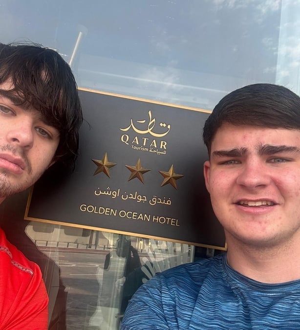 two young men smile for the camera with a hotel sign in the background